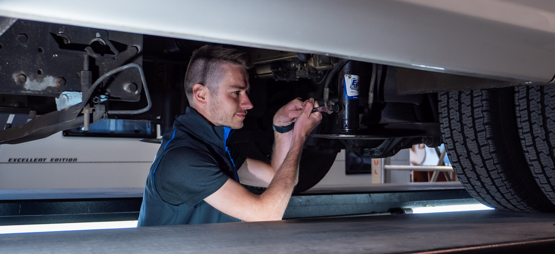 Werkstattmitarbeiter von Caravaning Center Schmidtmeier bei der Arbeit an einem Wohnmobil auf einer Hebebühne.